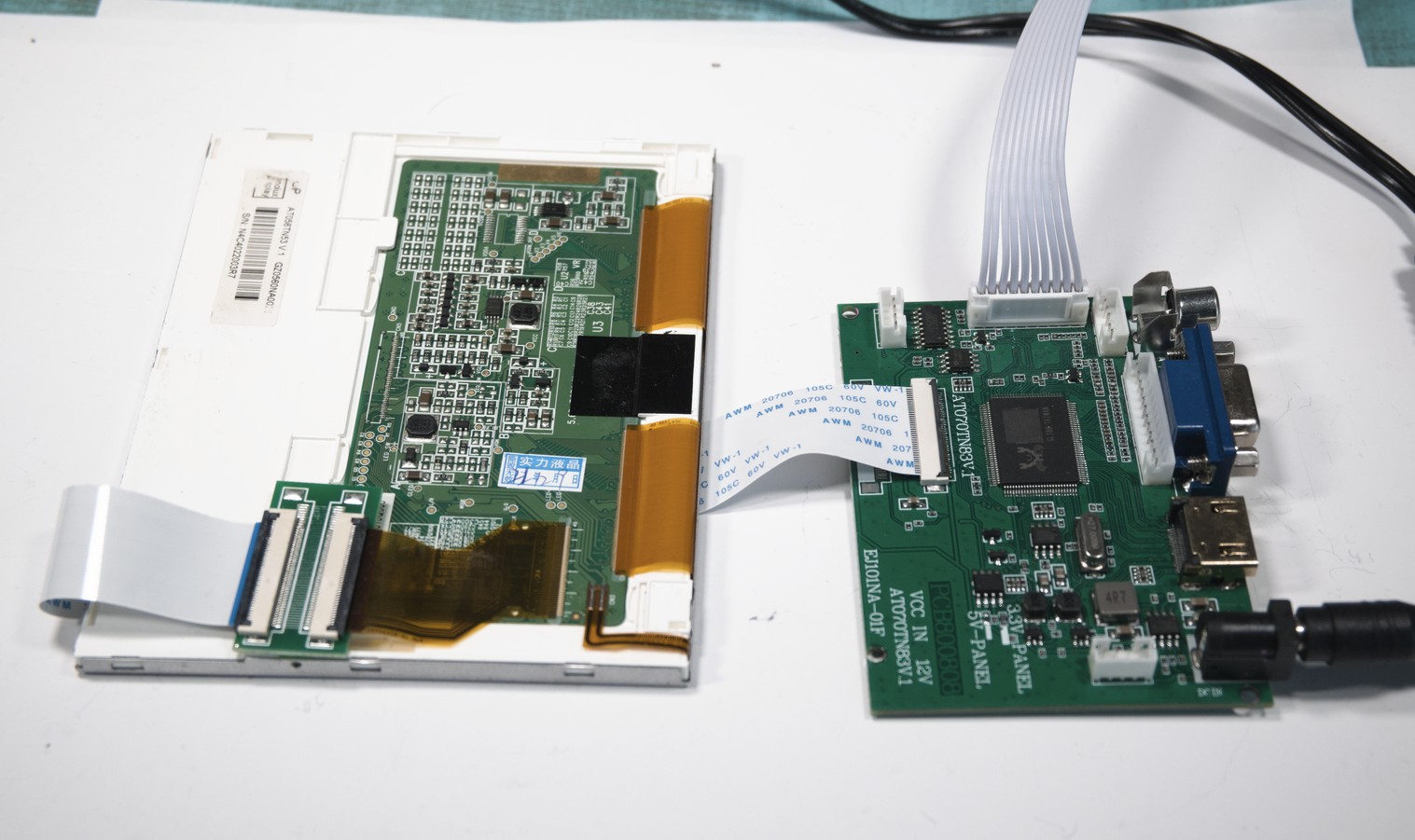 The LCD panel is backed by white plastic, and has a small PCB attached with a ribbon cable. The ribbon cable connects to the controller PCB, which has connectors for video input and power.