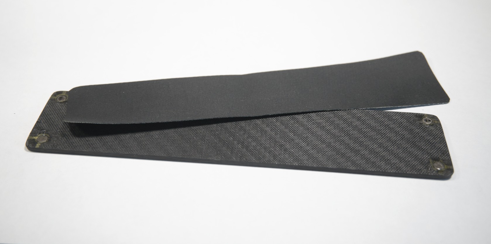 A sheet of carbon fibre the same size as the box. In each corner is a small disc-shaped magnet. Layed partly on top is a sheet of rubber the same size.
