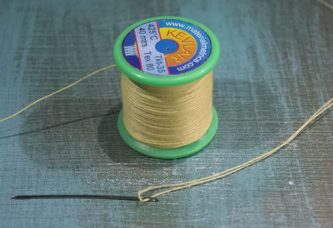 A bobbin of yellow Kevlar thread and a large needle.